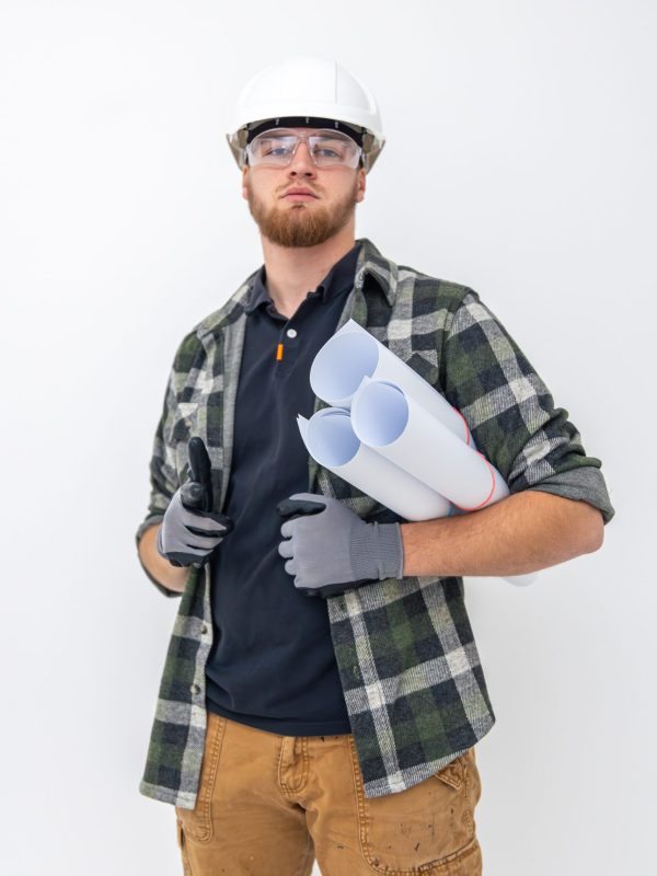 Male builder. Engineer in overalls and helmet holds blueprints and projects in his hands. Light background. Construction concept. Space for text. High quality photo